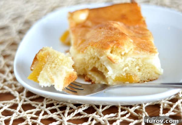 Sun-Kissed Peach Dream Cake 2 A beautifully presented slice of Peaches and Cream Cake with a bite taken out, revealing its luscious layers of tender cake, sweet peaches, and creamy topping, served on a white plate.