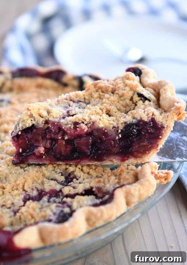 A delectable slice of triple berry rhubarb pie on a pie server, showcasing its rich filling and golden streusel.