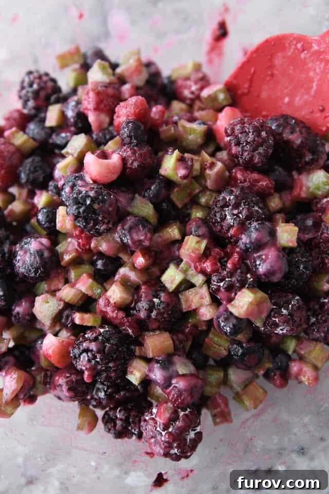 Freshly sliced rhubarb and a vibrant triple berry blend in a clear glass bowl, ready for the pie filling.