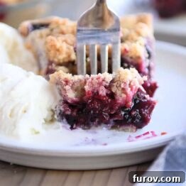 Fork taking a bite of berry rhubarb pie and vanilla ice cream on a gray plate, a perfect dessert moment.