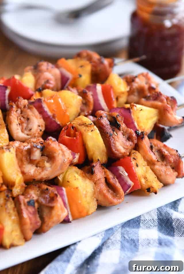 Aloha Chicken Pineapple Kabobs 2 Four perfectly grilled chicken, pineapple, and onion skewers resting on a pristine white platter, showcasing their golden-brown char and vibrant colors.