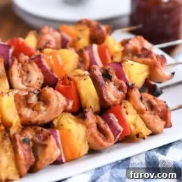 Several chicken, pineapple, and bell pepper skewers artfully arranged on metal sticks, presented on a clean white platter, showcasing their appealing grill marks and colorful ingredients.