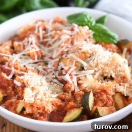 Serving of chicken zucchini Italian skillet in white bowl with parmesan cheese and fresh basil.