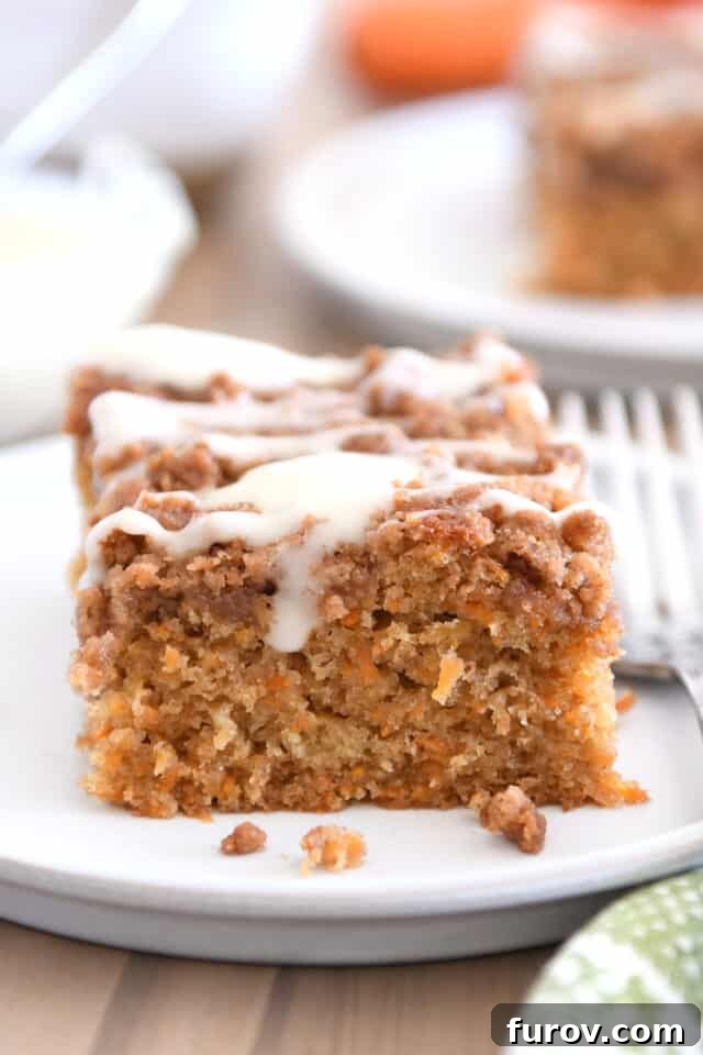 Square of carrot cake coffee cake drizzled with cream cheese glaze on white plate with fork. A perfect blend of sweet and tangy, highlighting the streusel topping.