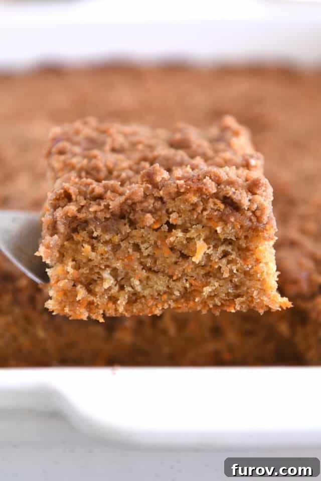 A perfectly baked square of carrot cake coffee cake resting on a metal spatula, showcasing its layers before glazing, highlighting its golden crust.