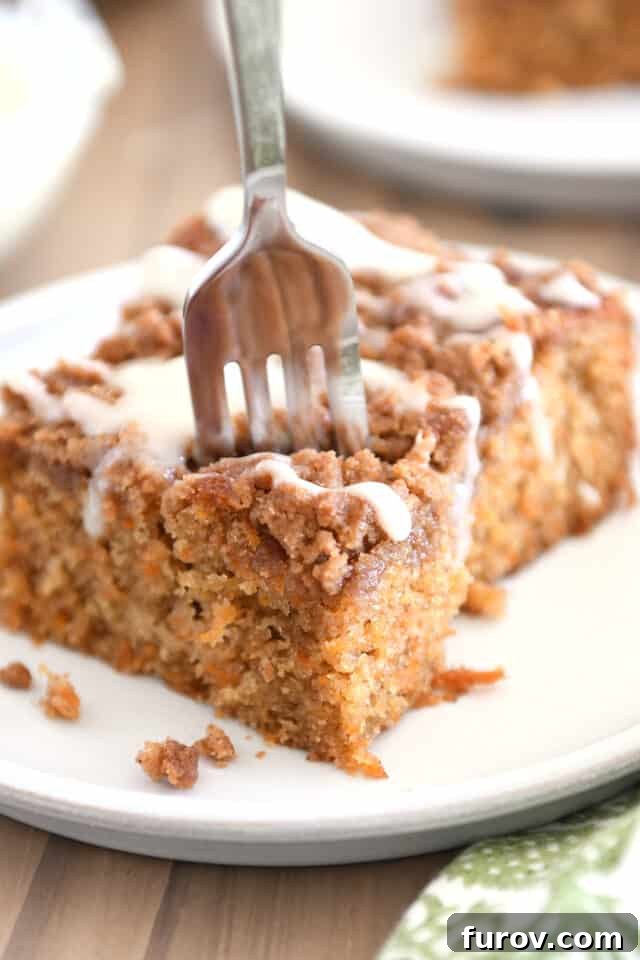Fork scooping a corner bite from a square of carrot cake coffee cake, revealing the moist interior and crumbly streusel.