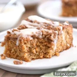 Bite taken out of carrot cake coffee cake on light gray plate, showcasing its moist texture and streusel topping.