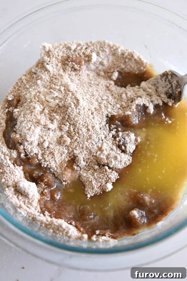 Melted butter being added to the dry streusel ingredients in a glass bowl, initiating the mixing process.
