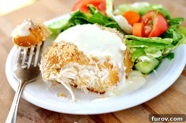 A chicken pillow cut open, revealing the creamy chicken filling inside, served on a white plate with a side salad.