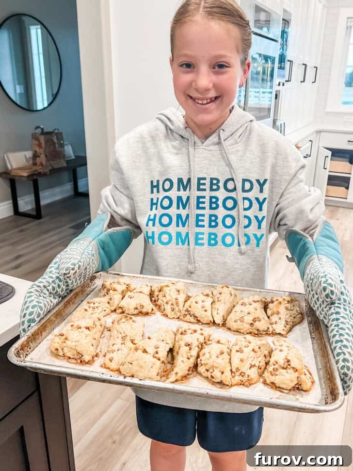 A young girl proudly holding a tray laden with freshly baked, delicious-looking scones.