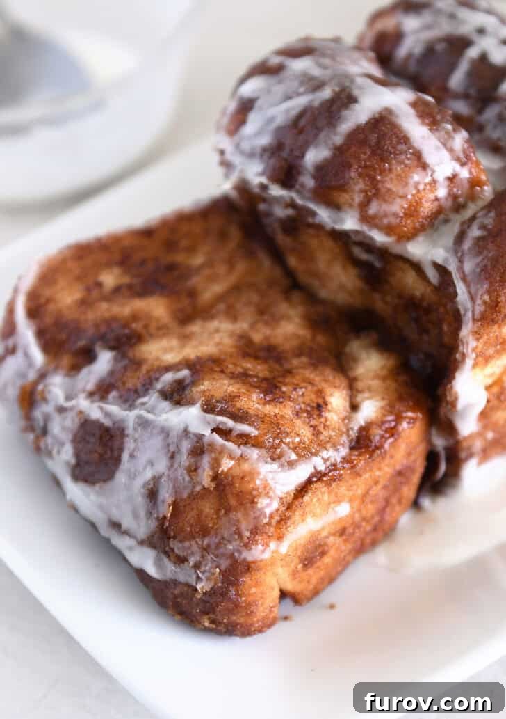 Thick slice of glazed cinnamon pull-apart bread with loaf on white platter.