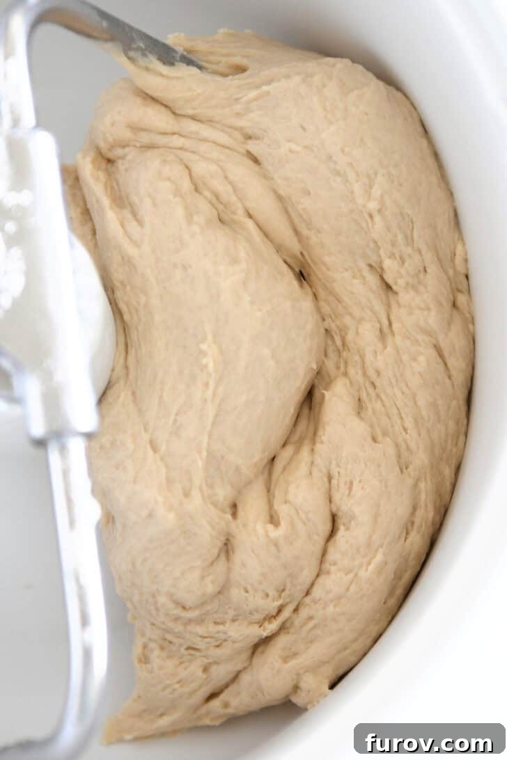 Smooth bread dough rising in a stand mixer bowl.