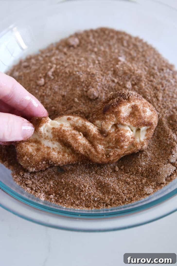 Rolling buttered piece of dough in brown sugar and cinnamon mixture.