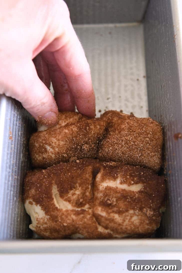 Placing slices of cinnamon and sugar coated dough in loaf pan for baking.