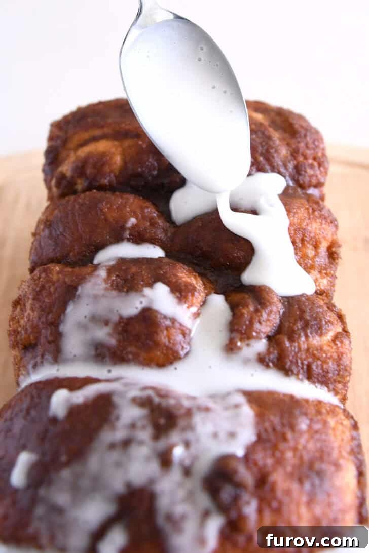 Drizzling powdered sugar glaze with spoon over top of cinnamon pull-apart bread.