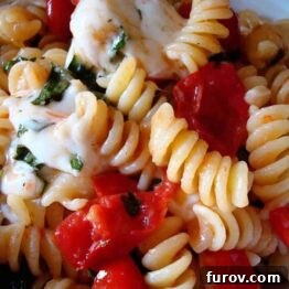 A small bowl of Fusilli alla Caprese, highlighting the pasta spirals, red tomatoes, and green basil.
