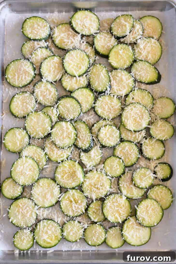 Thinly sliced zucchini rounds on a half sheet pan, evenly topped with Panko bread crumbs and grated Parmesan cheese.