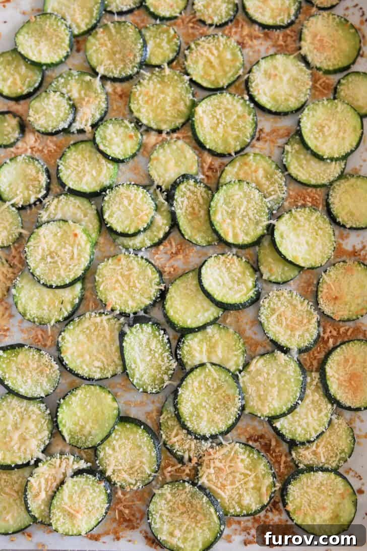 Baked golden zucchini rounds fresh from the oven on a half sheet pan, with a perfectly crispy bread crumb and Parmesan cheese topping.