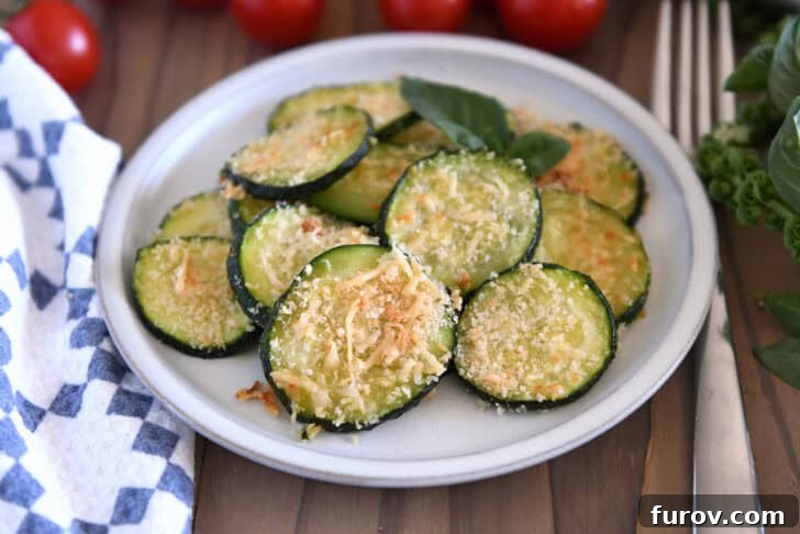 Thinly sliced baked zucchini rounds artfully arranged on a plate, showcasing their golden-brown, crispy Panko bread crumb and Parmesan cheese topping.