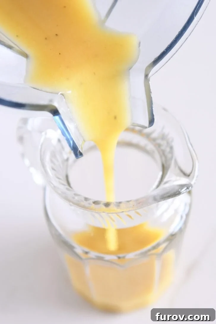 A steady stream of golden apple cider vinaigrette being poured into a clear glass jar, illustrating its smooth texture and readiness for storage or serving.