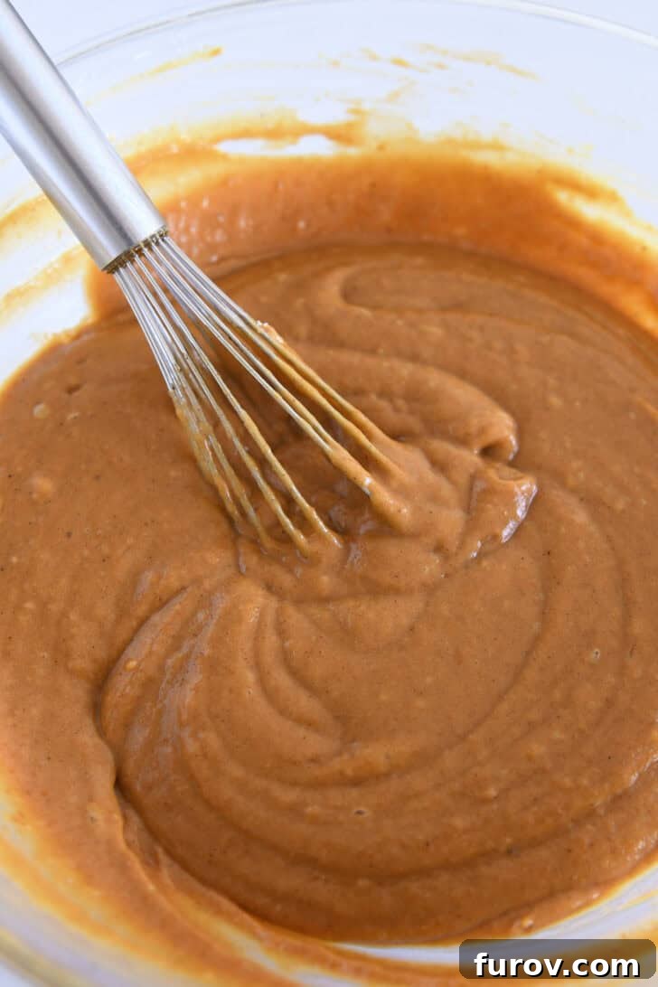 Pumpkin cupcake batter in glass bowl with wire whisk.