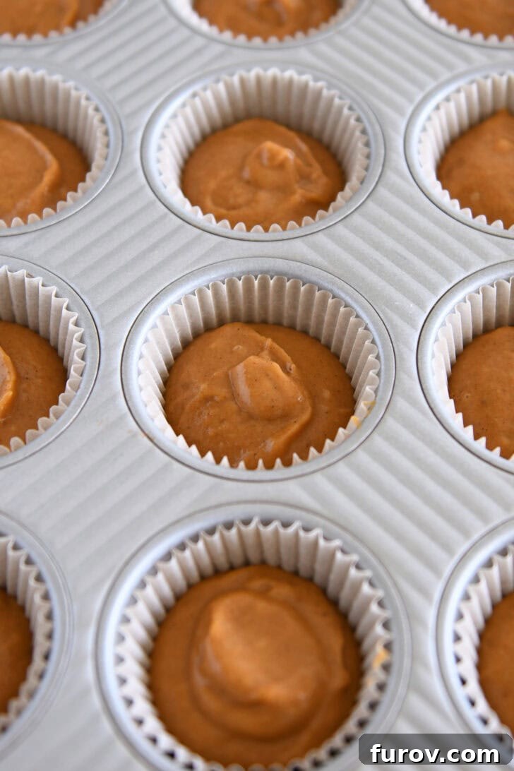 Metal cupcake tin with liners filled with pumpkin cupcake batter.
