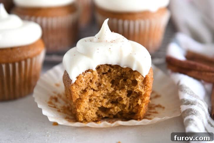 Pumpkin cupcake topped with whipped cream cheese frosting with bite taken out on unwrapped cupcake liner.