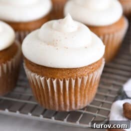 Several pumpkin cupcakes topped with whipped cream cheese frosting on wire cooling rack.