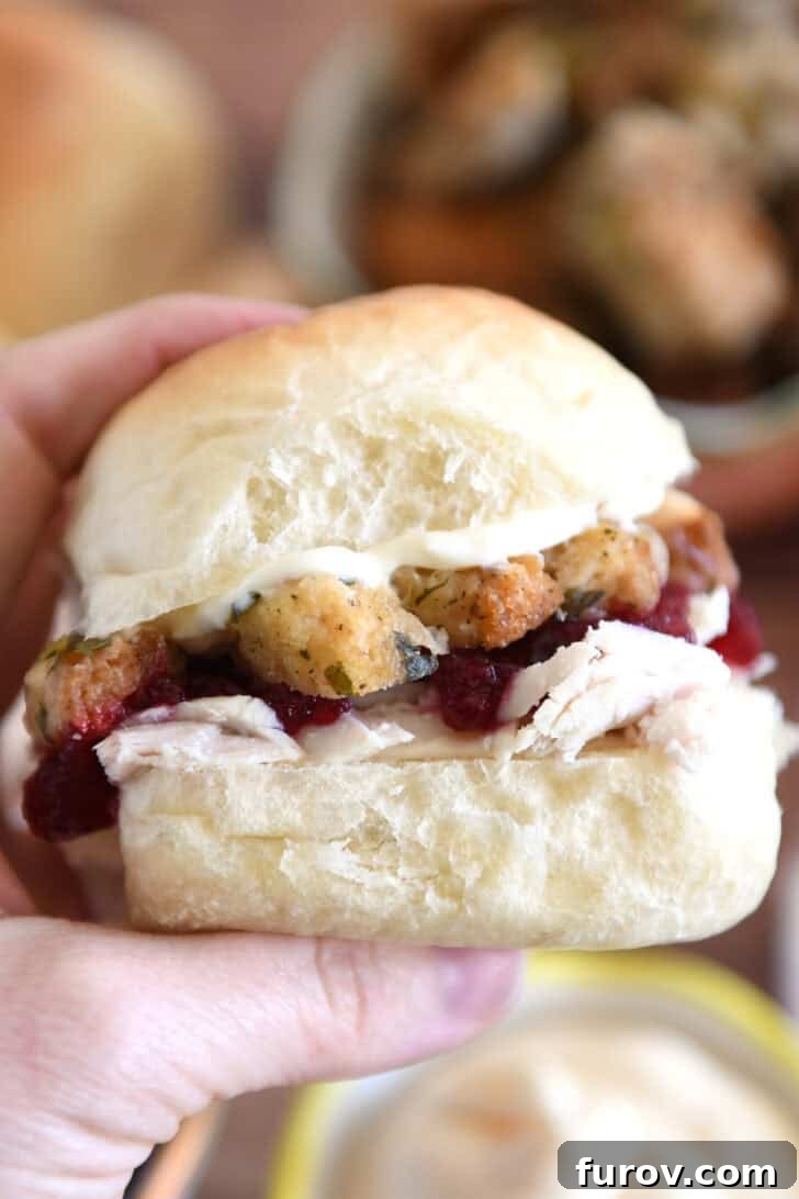 The Ultimate Leftover Turkey Sandwich: Restaurant Favorite At Home 2 Holding homemade roll sandwiched with mayonnaise, stuffing, cranberry sauce and shredded turkey between fingers.