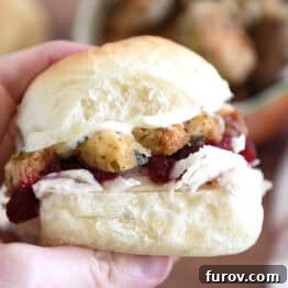 The Ultimate Leftover Turkey Sandwich: Restaurant Favorite At Home 9 Holding homemade roll sandwiched with mayonnaise, stuffing, cranberry sauce and shredded turkey between fingers.