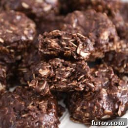 Stack of chocolate no-bake cookies on white plate with one cookie broken in half.