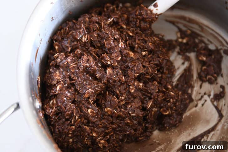 Irresistible No-Bake Chocolate Cookies 7 Saucepan filled with chocolate no-bake cookie batter, ready for scooping, with a white rubber spatula.