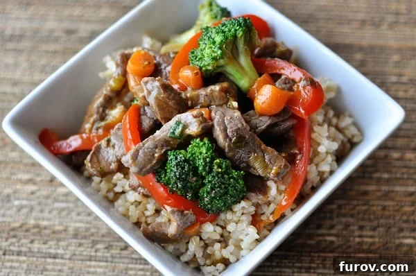 Sizzling Orange-Glazed Beef and Vegetable Medley 2 Top view of a square white bowl with cooked rice, veggies and strips of beef.