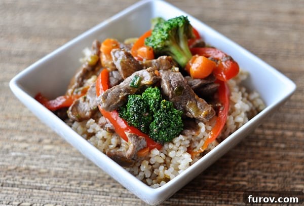 Sizzling Orange-Glazed Beef and Vegetable Medley 3 Square white bowl with cooked rice topped with cooked broccoli and peppers and beef strips.