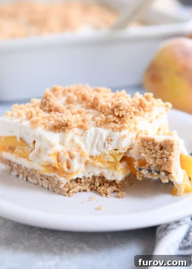 No-Bake Peaches and Cream Bliss 6 A fork taking a bite out of a square piece of peaches and cream dessert on a white plate, showing the creamy texture and peach slices.