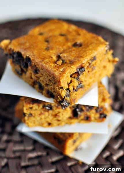 Autumn Spice Pumpkin Chocolate Chip Blondies 3 A stack of perfectly baked pumpkin chocolate chip blondies nestled on pieces of parchment paper, ready to be enjoyed.