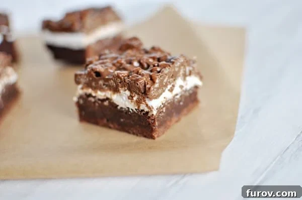 A small square chocolate bar cut to show the brownie bottom, marshmallow middle, and crunchy top layers.