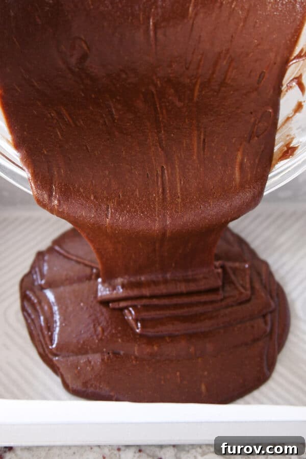 Pouring rich brownie batter into a parchment-lined 9x13-inch baking pan.