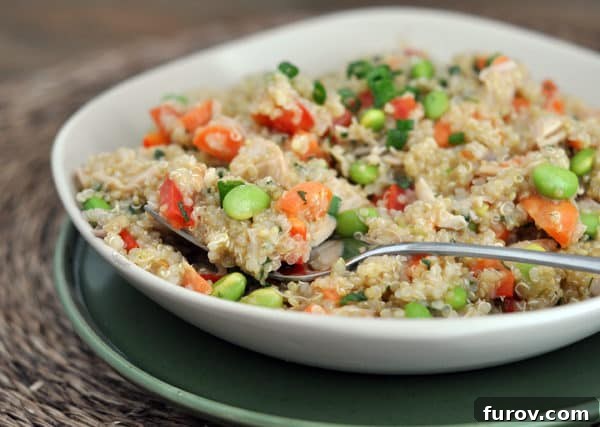 White bowl of cooked quinoa salad with edamame, peppers, and green onions.