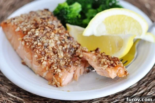 A white plate with a pecan crusted fillet of salmon, lemon wedges, and broccoli.