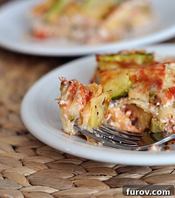 A fork taking a bite from a cheesy slice of zucchini lasagna, showing gooey layers.