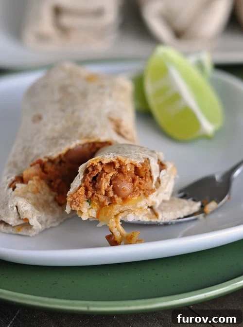 A fork cutting a bite out of a cooked beef and bean burrito on a white plate, showing the rich filling.