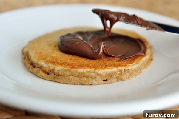 A pancake getting covered with Nutella.