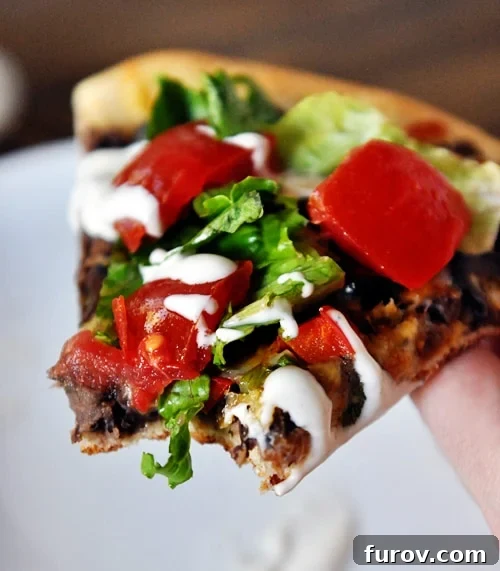 A slice of black bean pizza with a bite taken out and lettuce and tomatoes on top.