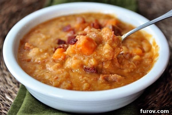 Hearty Slow Cooker Ham Sweet Potato White Bean Soup with Crispy Bacon 2 White bowl full of ham and veggie white bean soup with a spoon taking a bite out.