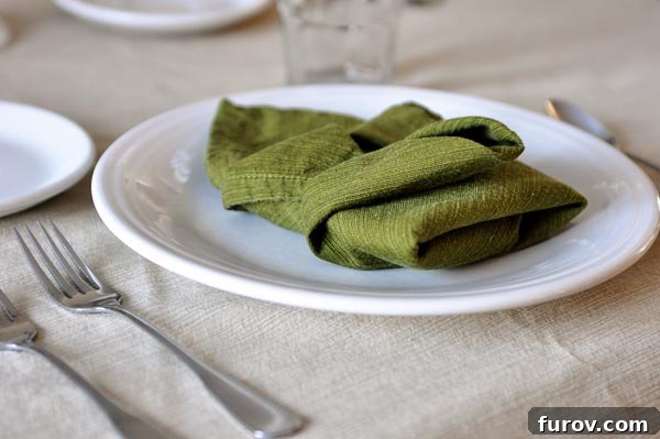 Your Guide to Perfect Family Candlelit Dinners Recipes and Atmosphere 8 A white plate with a elegantly folded green cloth napkin on top, showcasing a beautiful table setting.
