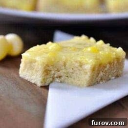 A close-up shot of a single Lemon Drop Sugar Cookie Bar, highlighting its glistening, perfectly set glaze and soft, crumbly texture.