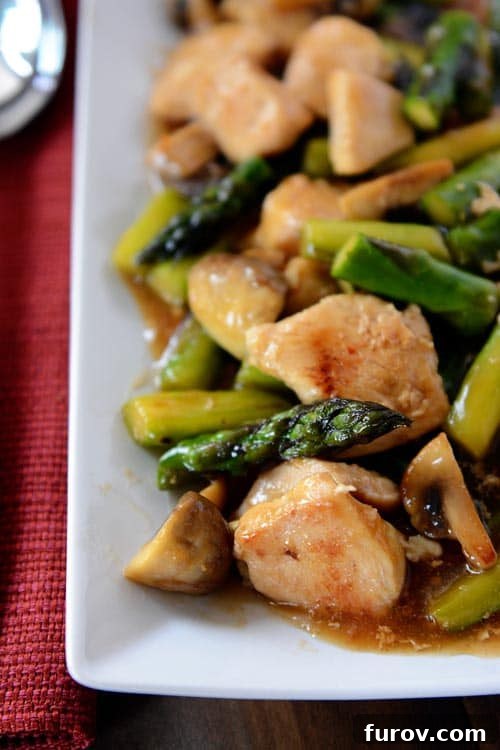 A long white platter filled with ginger chicken and asparagus stir fry covered in a rich sauce, ready to be served.