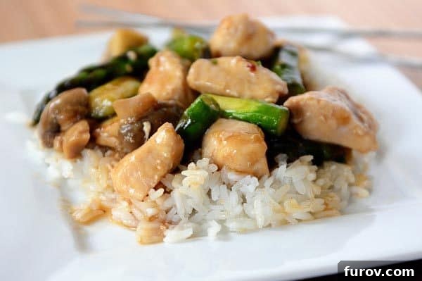A plate full of fluffy white rice topped generously with ginger chicken and asparagus stir fry, showcasing a vibrant and appetizing meal.