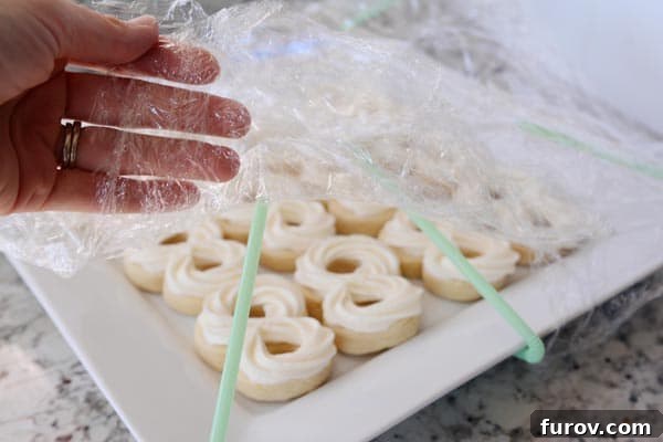Preserve the Beauty of Your Cupcakes and Cookies During Storage 2 Someone lifting up the side of a saran wrap to show a platter of frosted sugar cookies.